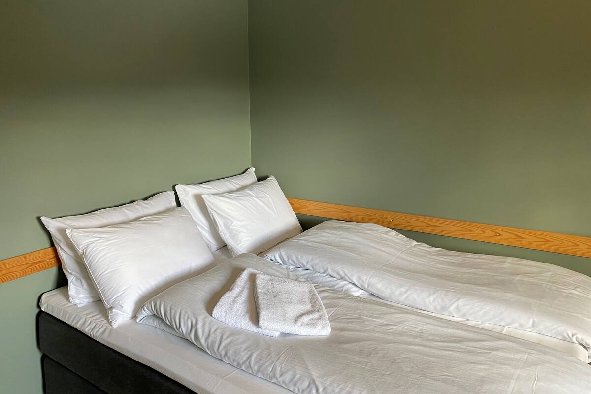 A neatly made bed with white linens and pillows, a wooden headboard, and a green wall.