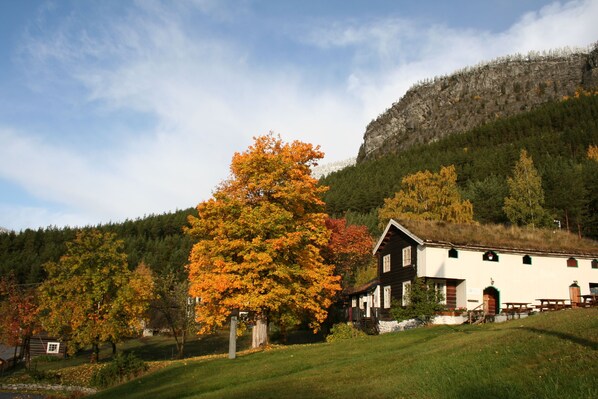 A rustic building with a sloped roof, surrounded by a grassy area and trees with autumn foliage.