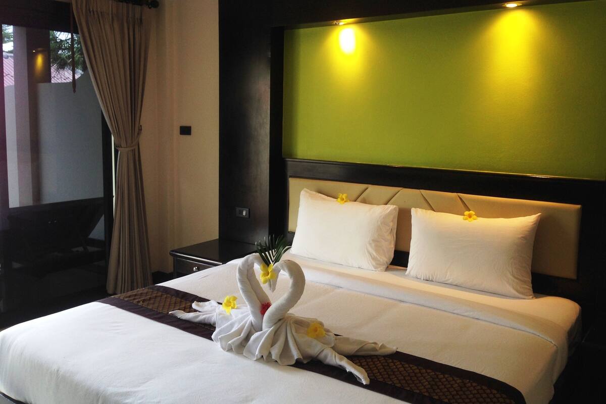 A hotel room with a neatly made bed, a green accent wall, and a swan-shaped towel decoration.