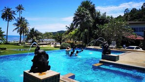 Une piscine agrémentée de statues décoratives, entourée de palmiers et offrant une vue sur l’océan.