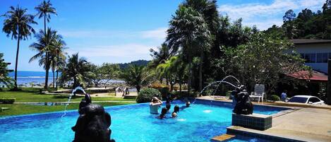 A swimming pool with decorative statues, surrounded by palm trees and a view of the ocean.