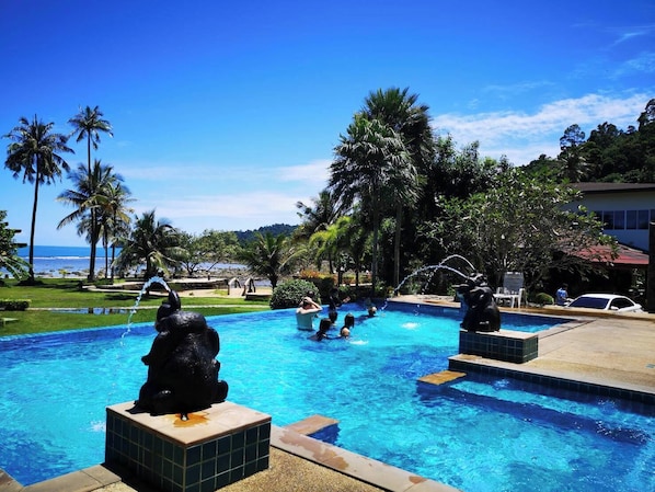 A swimming pool with decorative statues, surrounded by palm trees and a view of the ocean.