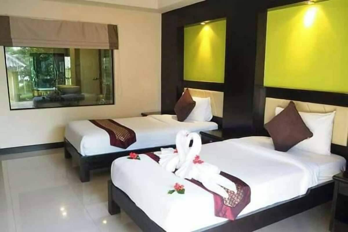 A hotel room with two beds, each with a swan decoration and a red rose. The room has a large window with a view of greenery outside.