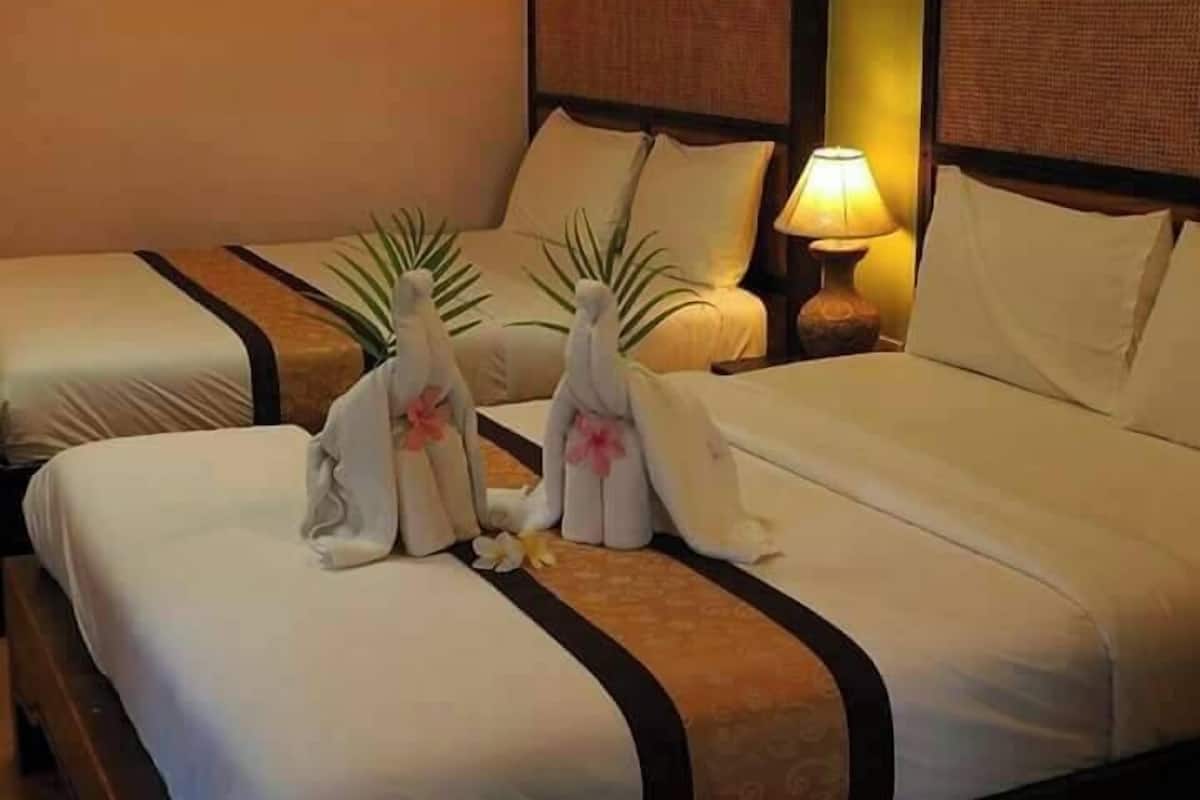 A hotel room with two beds, each with a neatly folded towel and a flower. There is a lamp on the nightstand beside the beds.