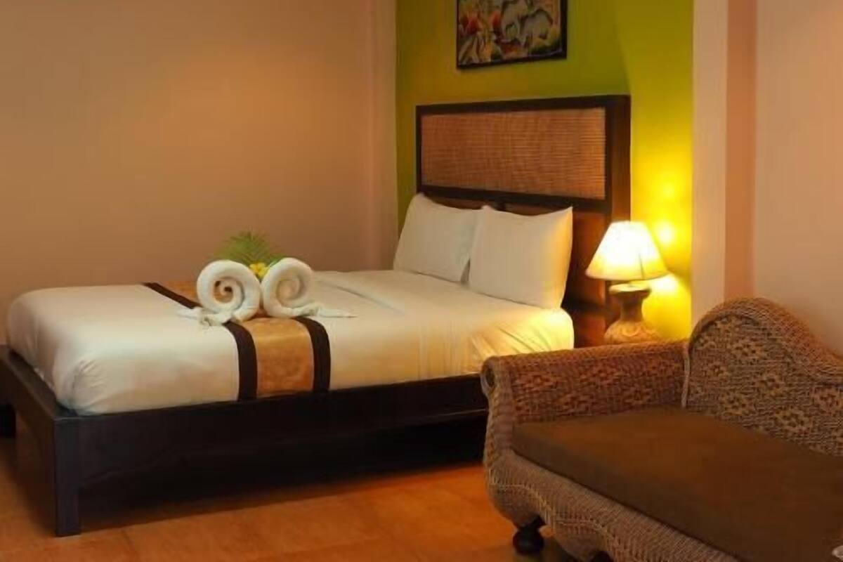 A hotel room with a bed, a nightstand with a lamp, a chair, and a painting on the wall.