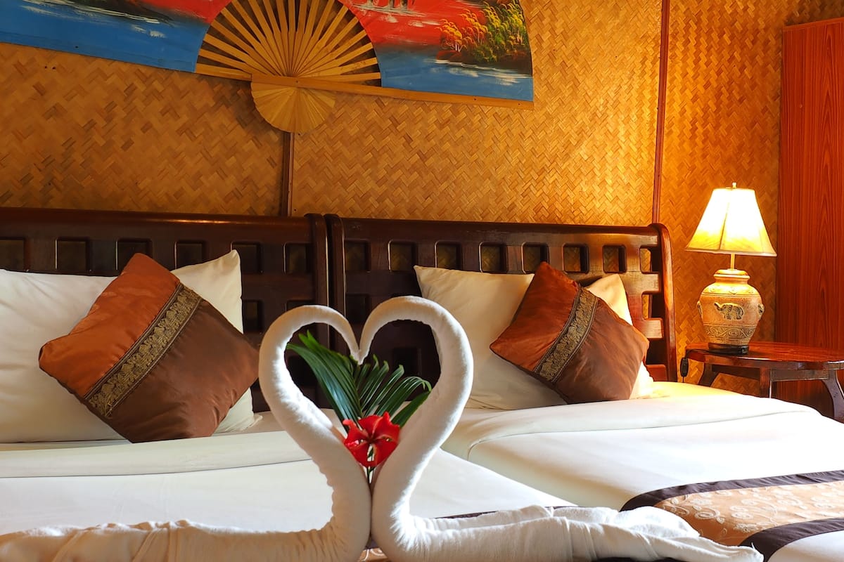 A hotel room with a bed featuring a heart-shaped towel arrangement and a painting above it.