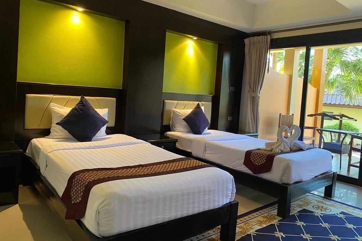 A hotel room with two beds, a balcony with a view, and a large window.
