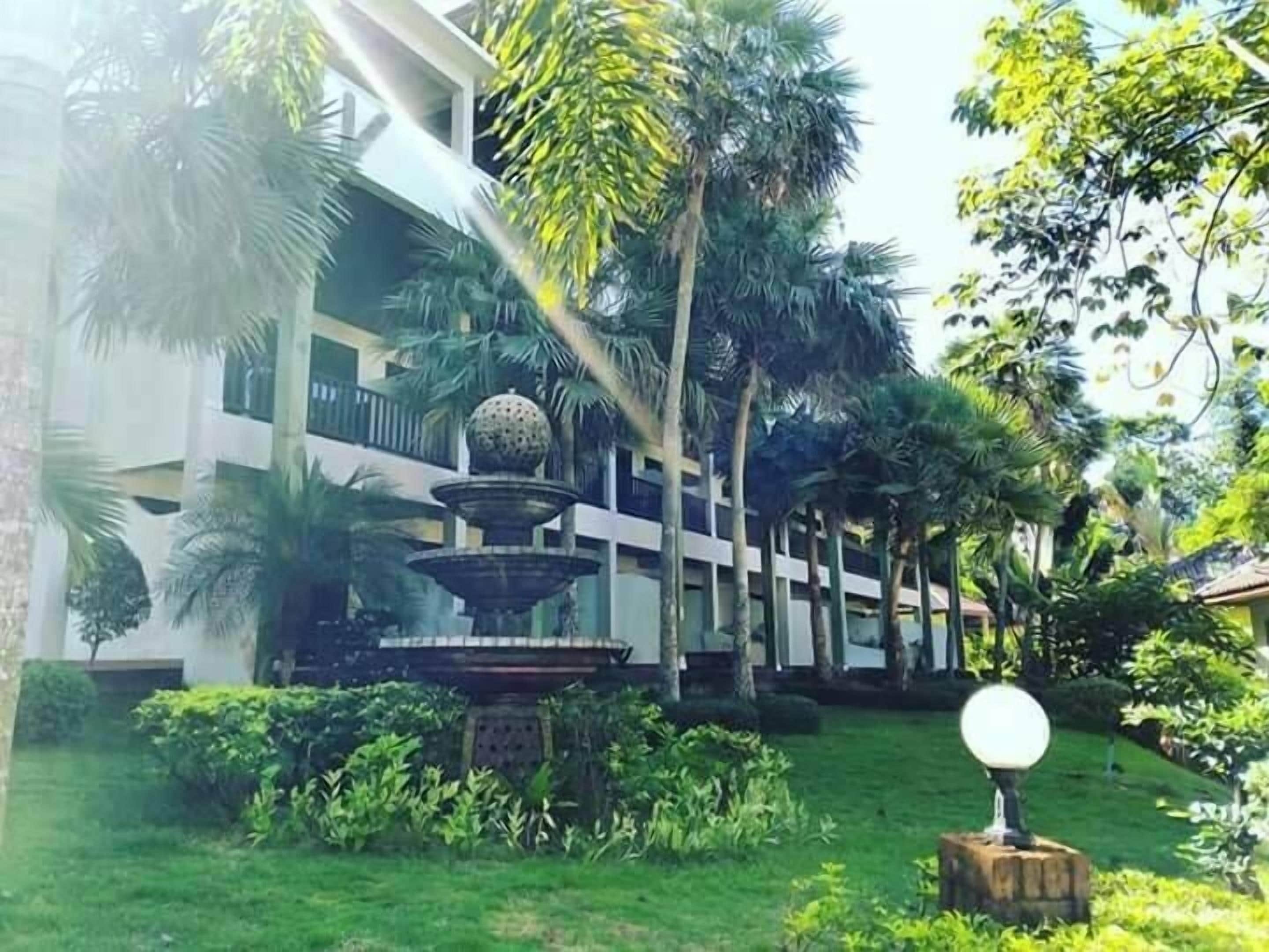 Un patio con una fuente escalonada, abundante vegetación y un edificio con balcones.