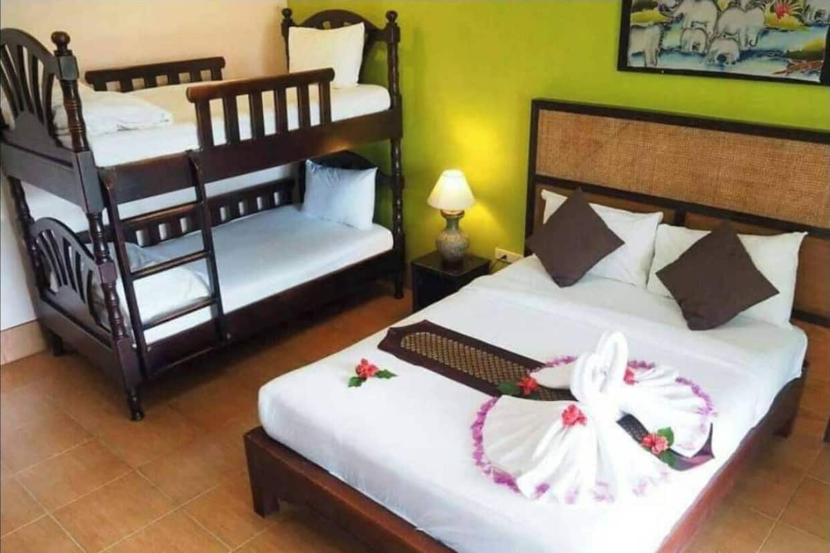 A hotel room with a bunk bed, a single bed with a towel and decorative pillow, and a nightstand with a lamp.