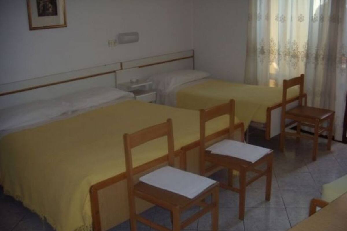 A hotel room with two single beds, a wooden chair, a small table, and a nightstand.