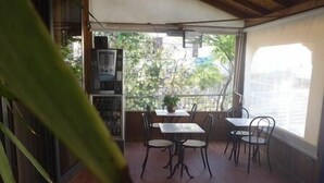 Un patio interior con suelo de madera, una mesa con sillas, una planta en maceta y una estantería.