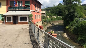 Un hotel con balcón, un río al fondo y un puente en primer plano.