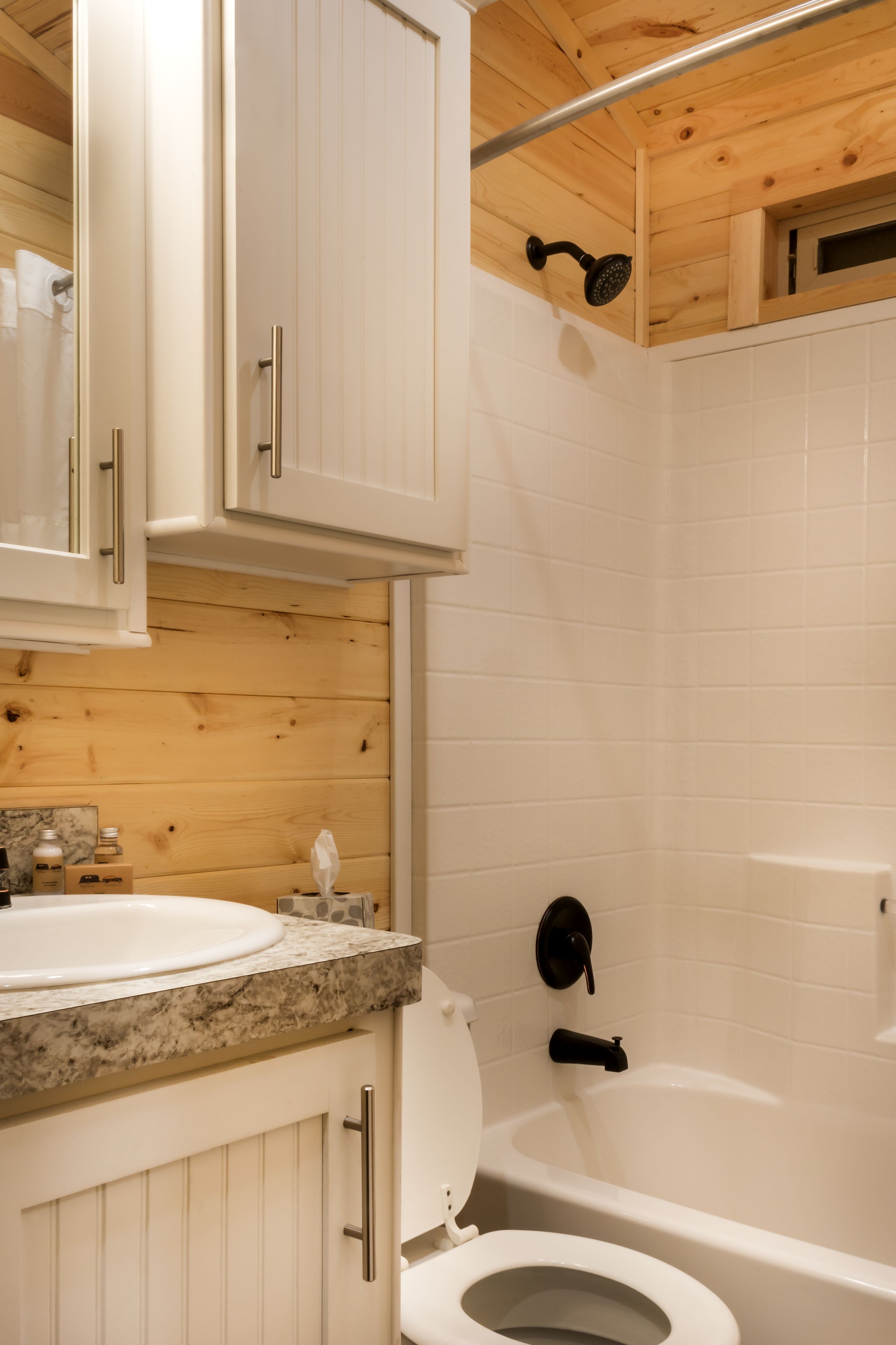 Un baño con techo de madera, azulejos blancos, un lavabo, un inodoro y una ducha.