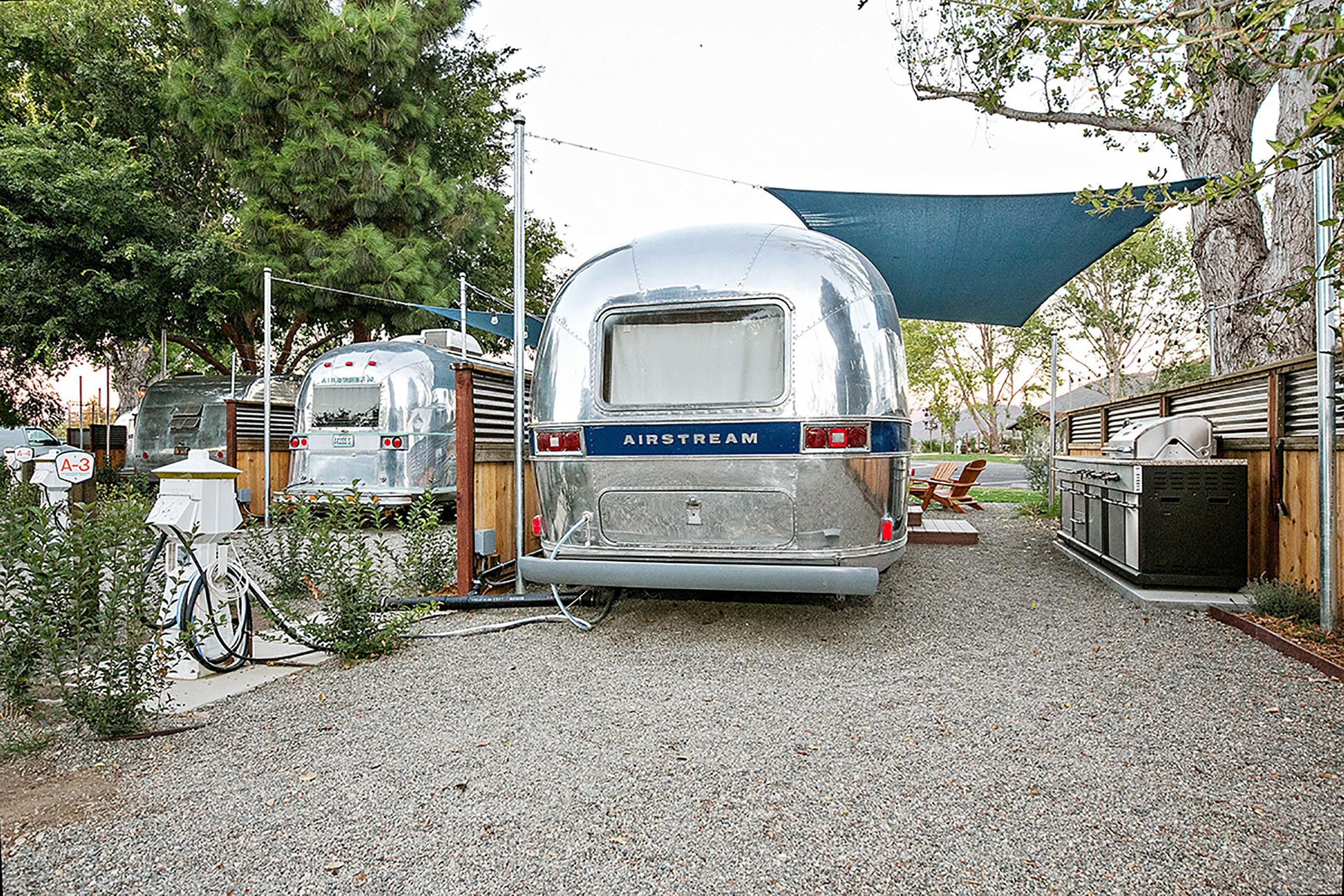 En husvagn med texten ”AIRSTREAM” parkerad på en grusplan, med ett tak över.