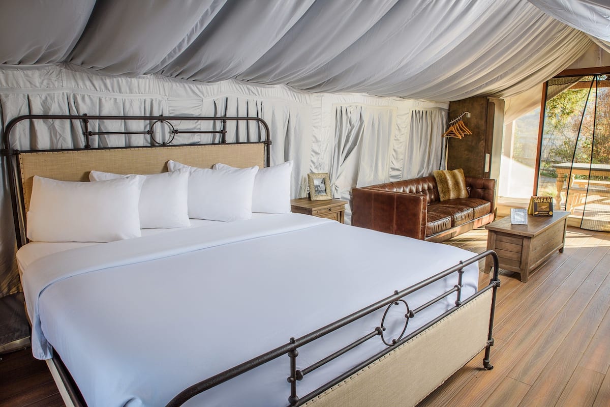 A spacious tented room with a large bed, a leather sofa, and a wooden nightstand.