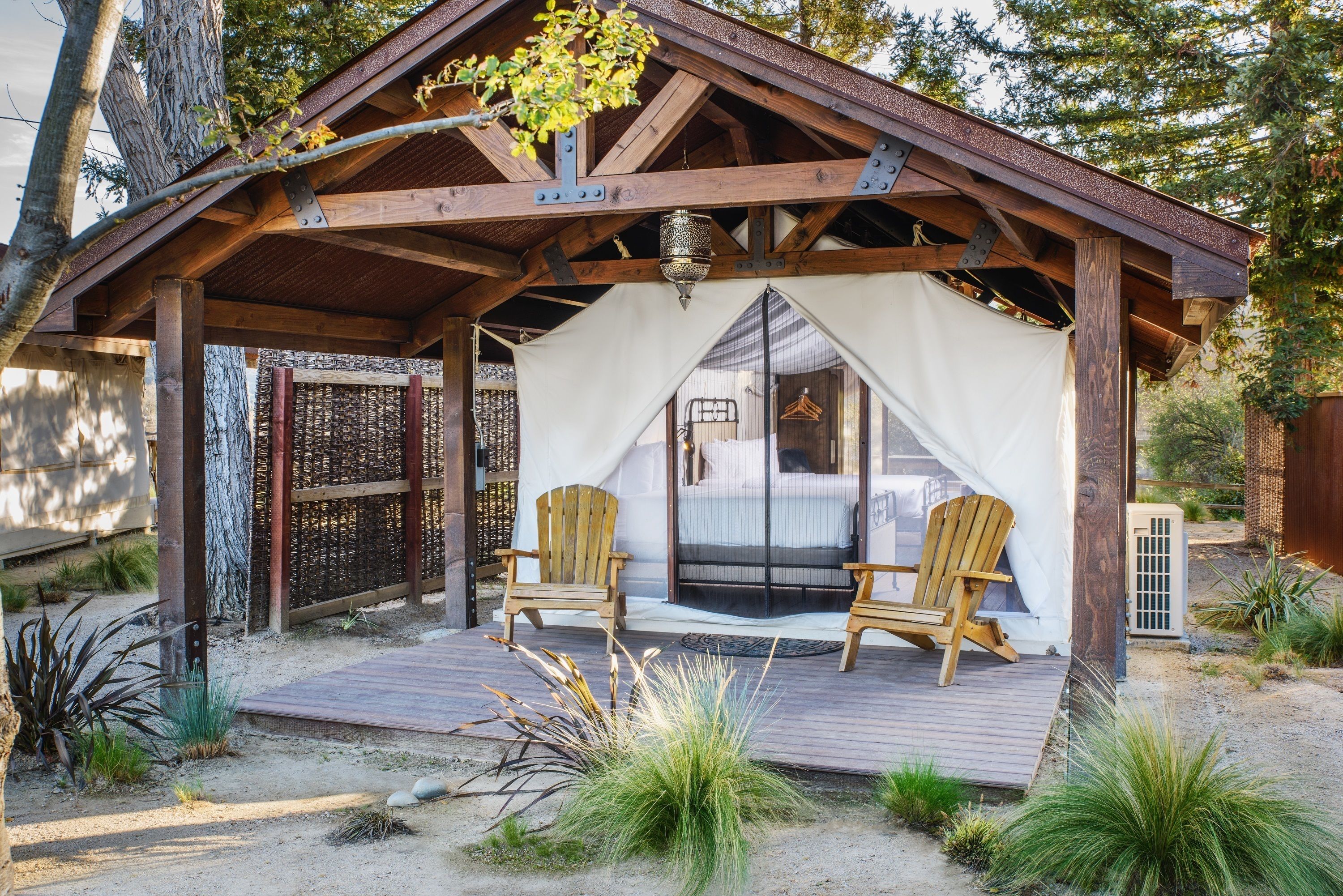 A wooden structure with a covered porch, two wooden chairs, and a bed with a white canopy.