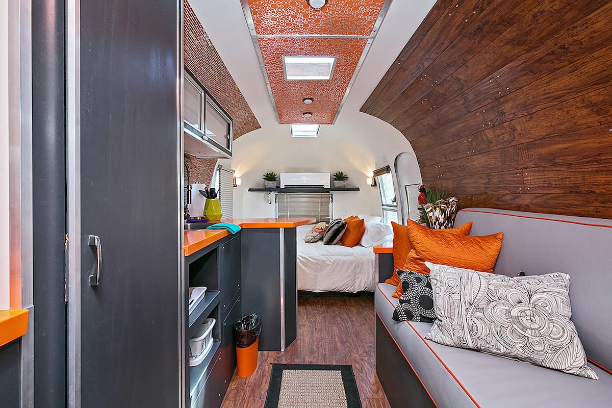 A compact RV interior with a kitchenette, a bed, and a seating area.