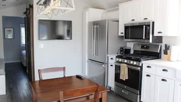 A modern kitchen with white cabinets, stainless steel appliances, and a wooden dining table.