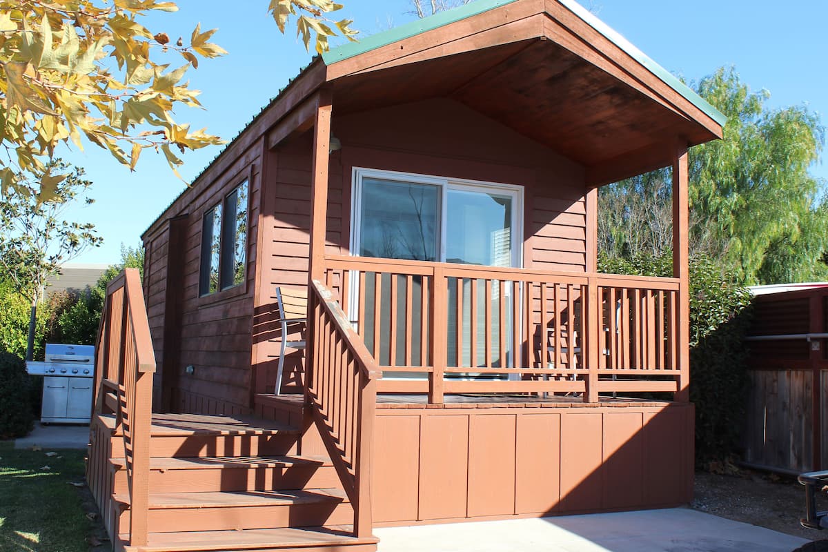 A wooden cabin with a balcony, a small porch, and a window.