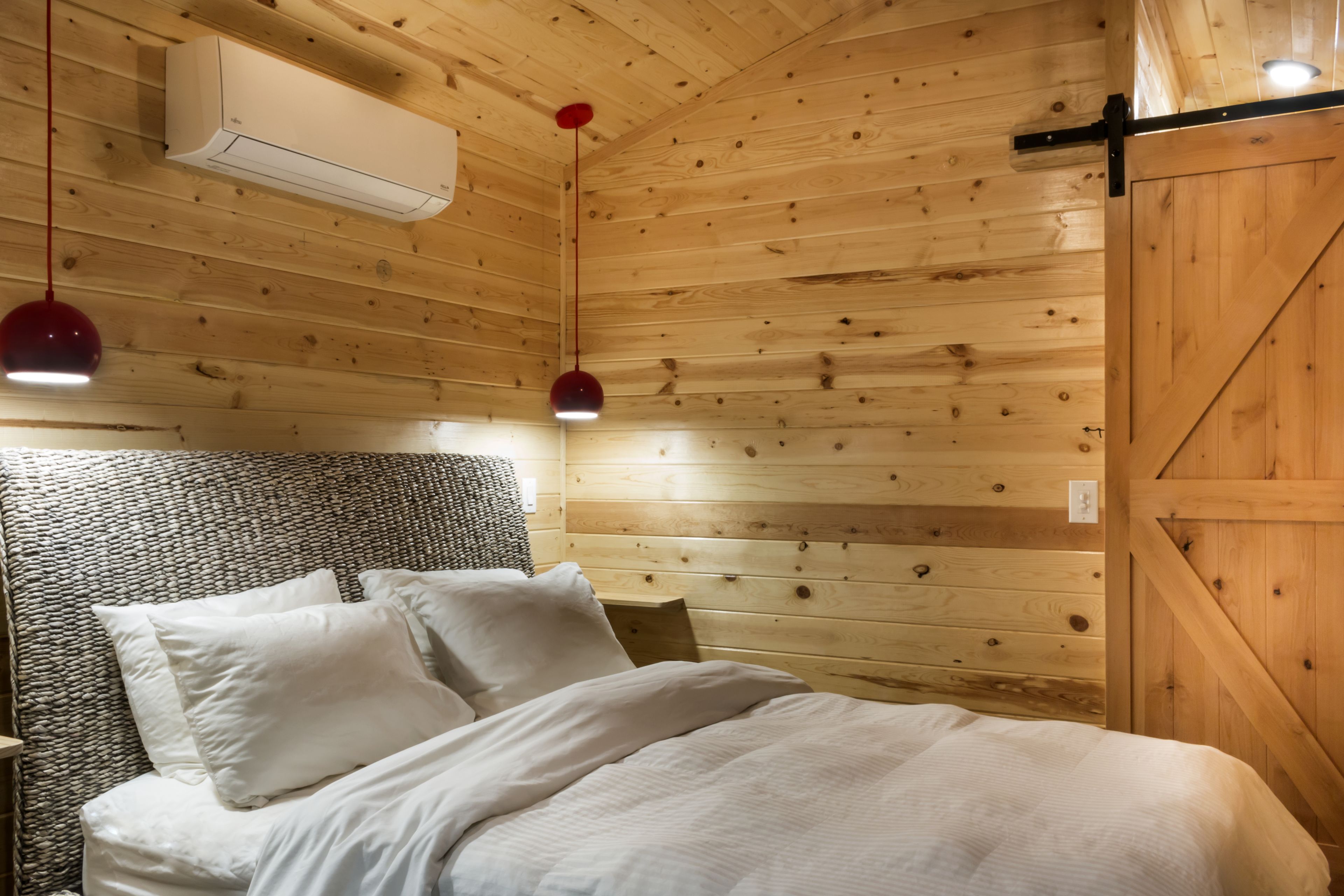 Une pièce aux murs lambrissés, comprenant un lit, deux lampes suspendues et un appareil de climatisation.