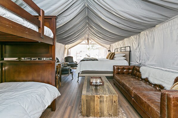 A tented room with a bunk bed, a single bed, a sofa, and a coffee table.