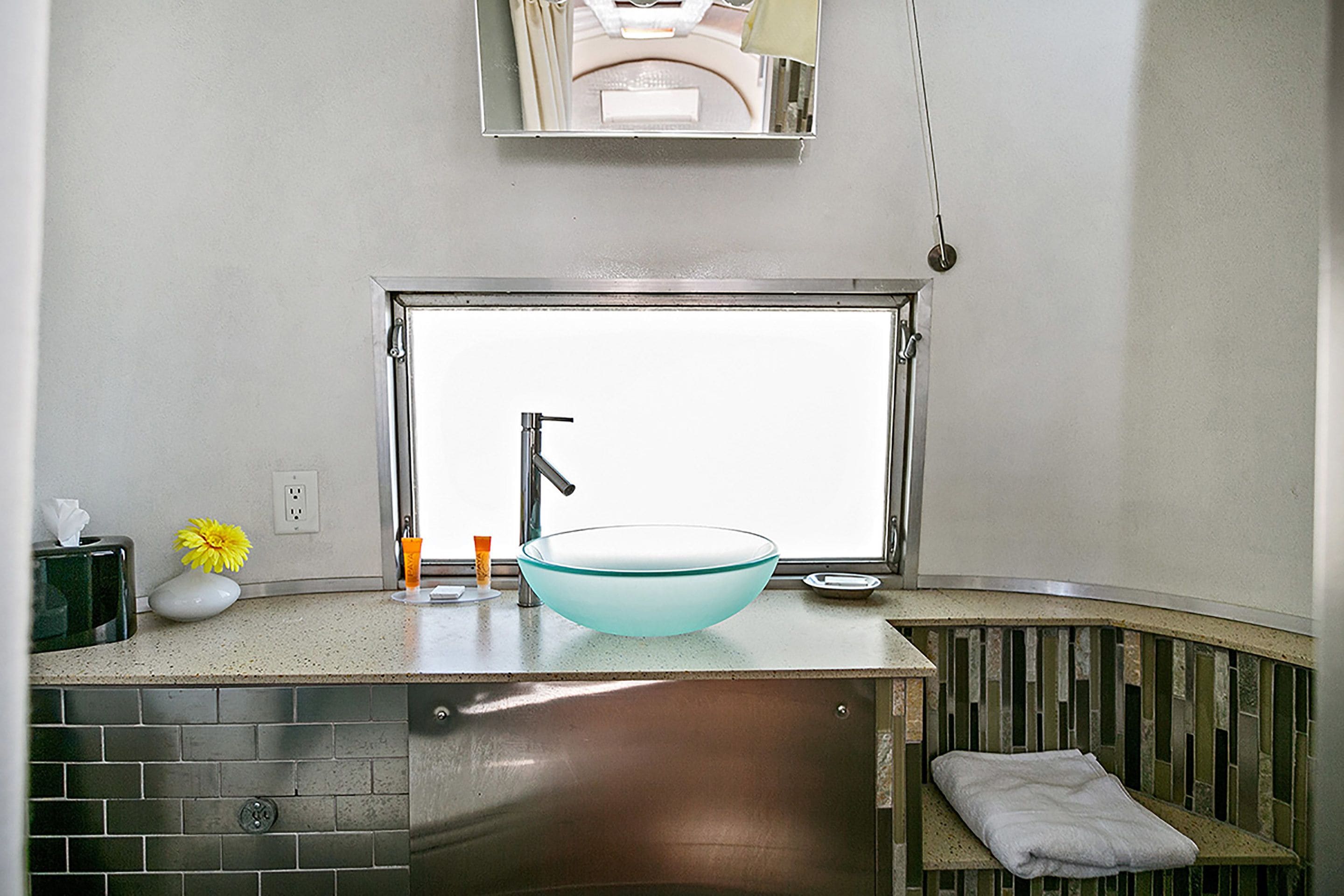 Un baño moderno con un ventanal grande, un lavabo de vidrio y un perchero para toallas.