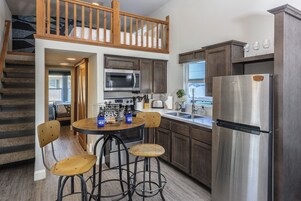 Una cocina moderna con un refrigerador de acero inoxidable, taburetes de bar de madera y un microondas integrado.