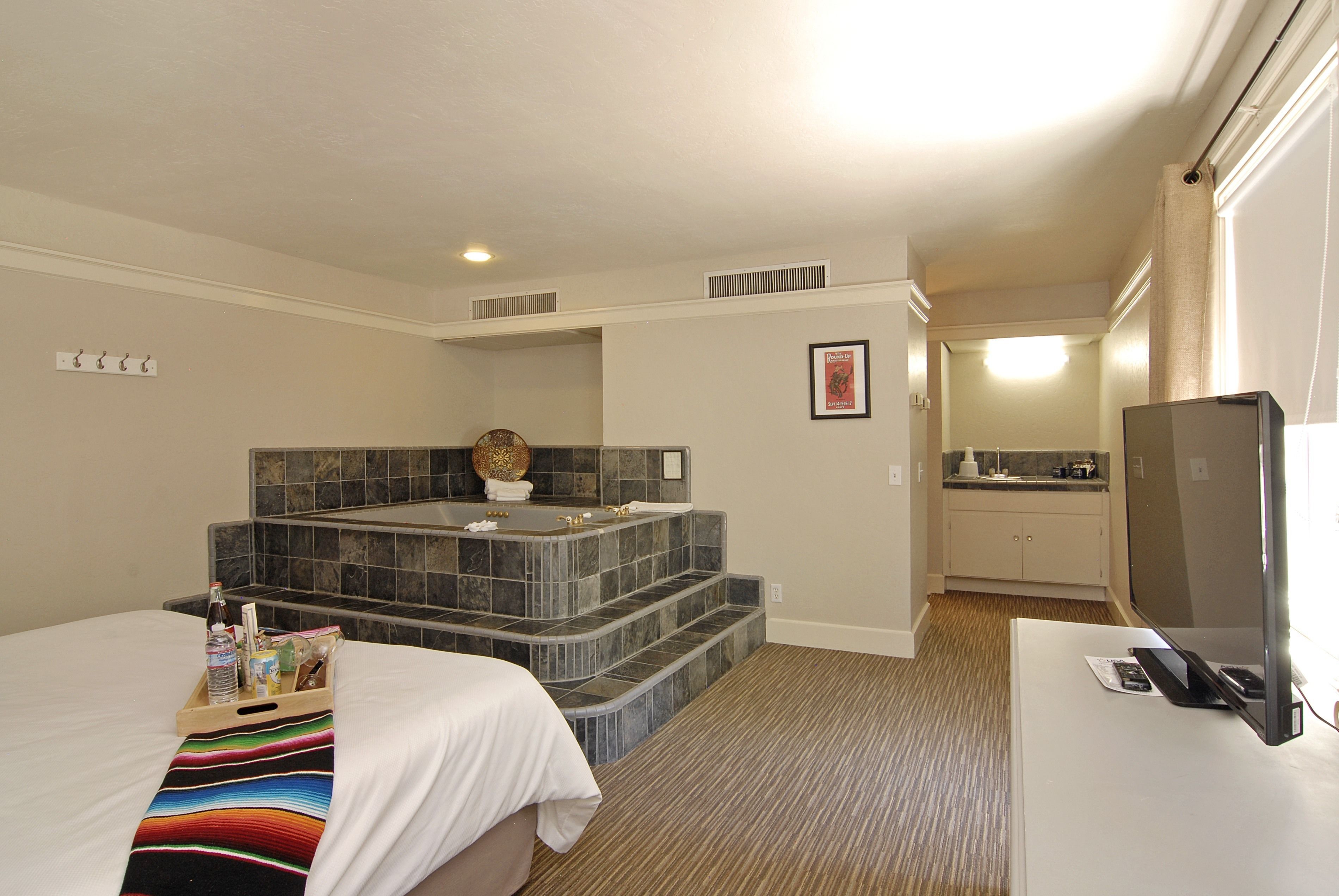 Een hotelkamer met een bed, een badkamer met een bad, een televisie en een kitchenette.
