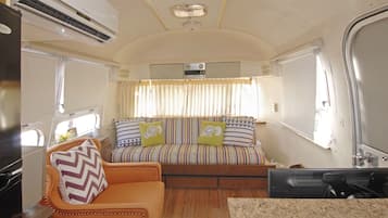 Interior compacto de autocaravana con cama, una zona de estar pequeña y una kitchenette.