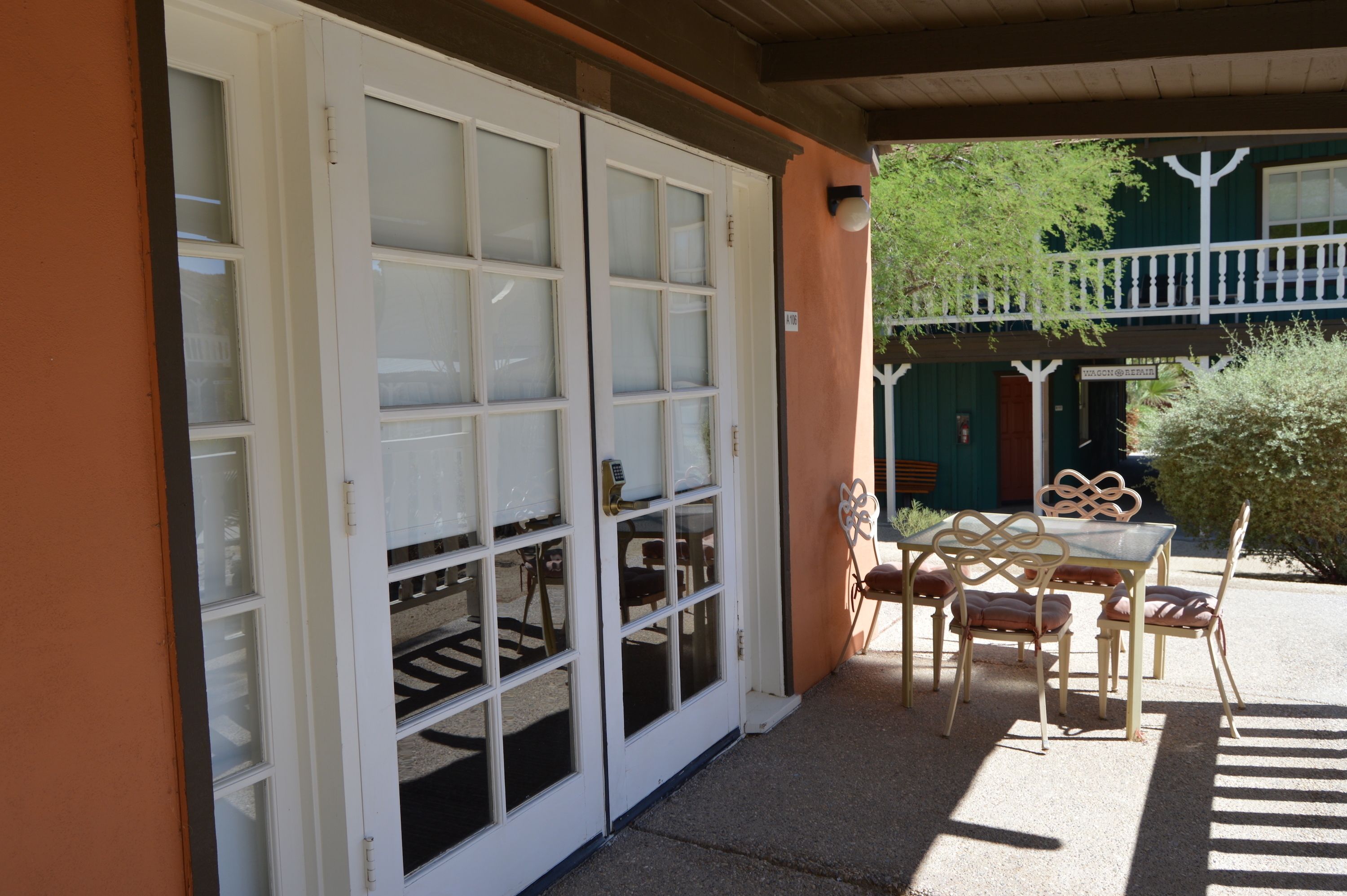 A covered patio with a table and chairs, a white door with glass panels, and a balcony with a railing.