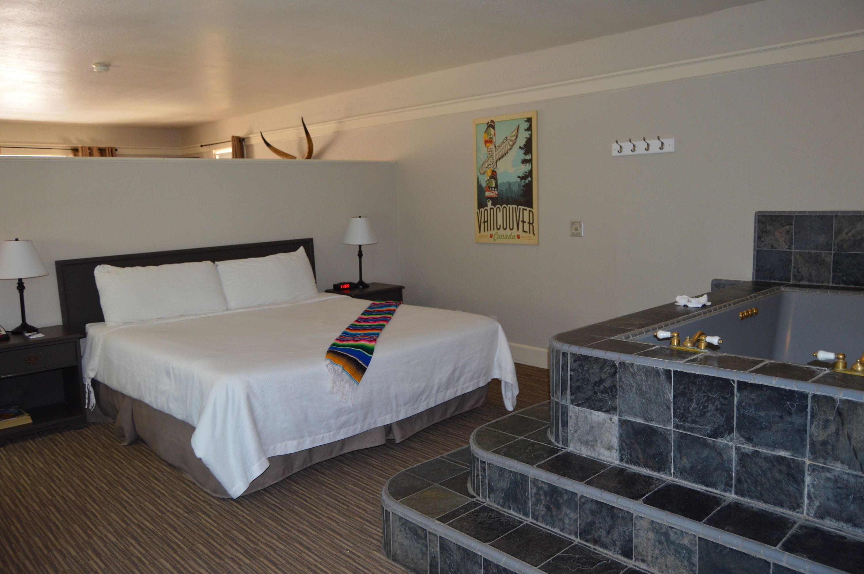 A hotel room with a large bed, a bathroom with a stone tub, and a poster on the wall.
