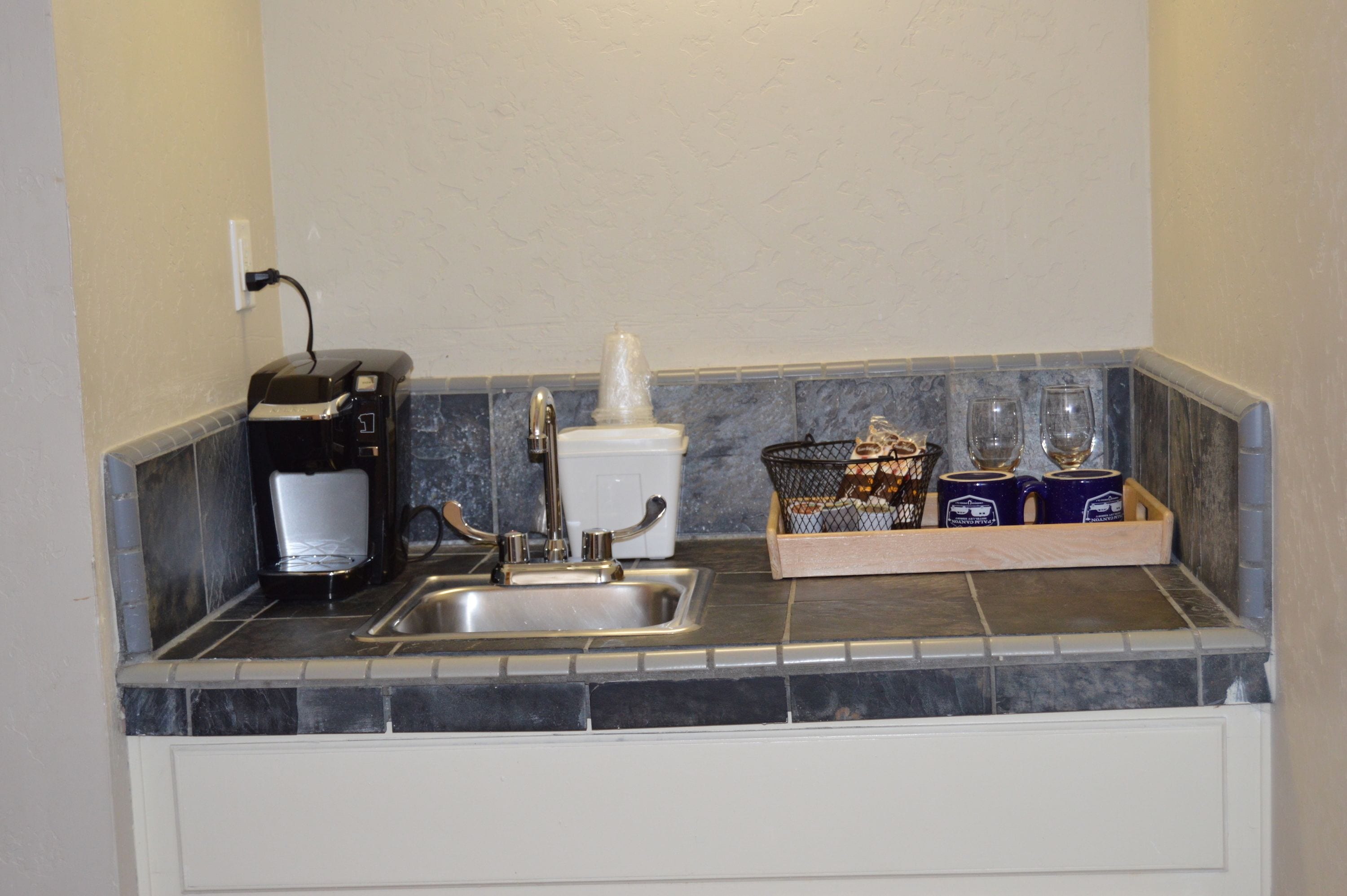 A kitchen with a coffee maker, a sink, and a tray with cups and glasses.