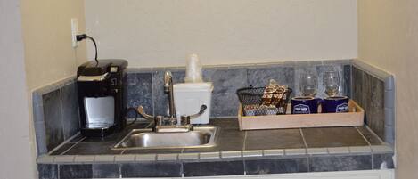 Una cocina con cafetera, un lavamanos y una bandeja con tazas y vasos.