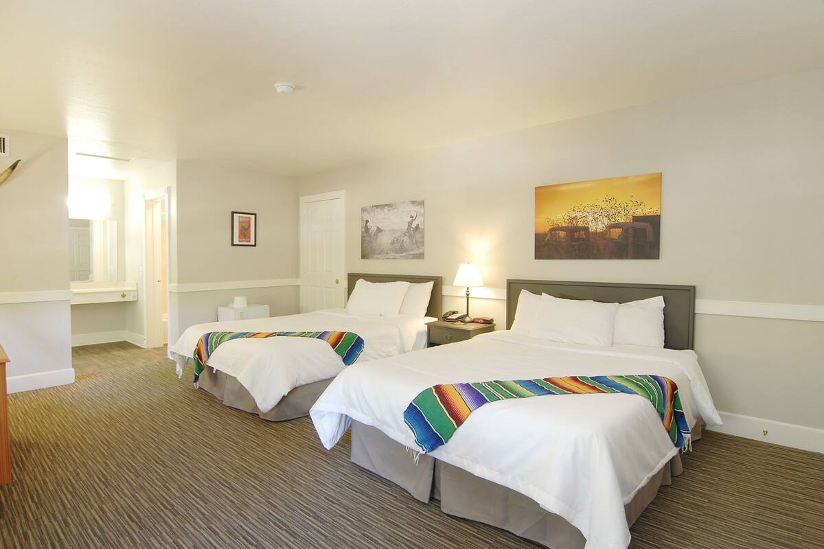 A hotel room with two beds, a nightstand, a lamp, and a painting on the wall.