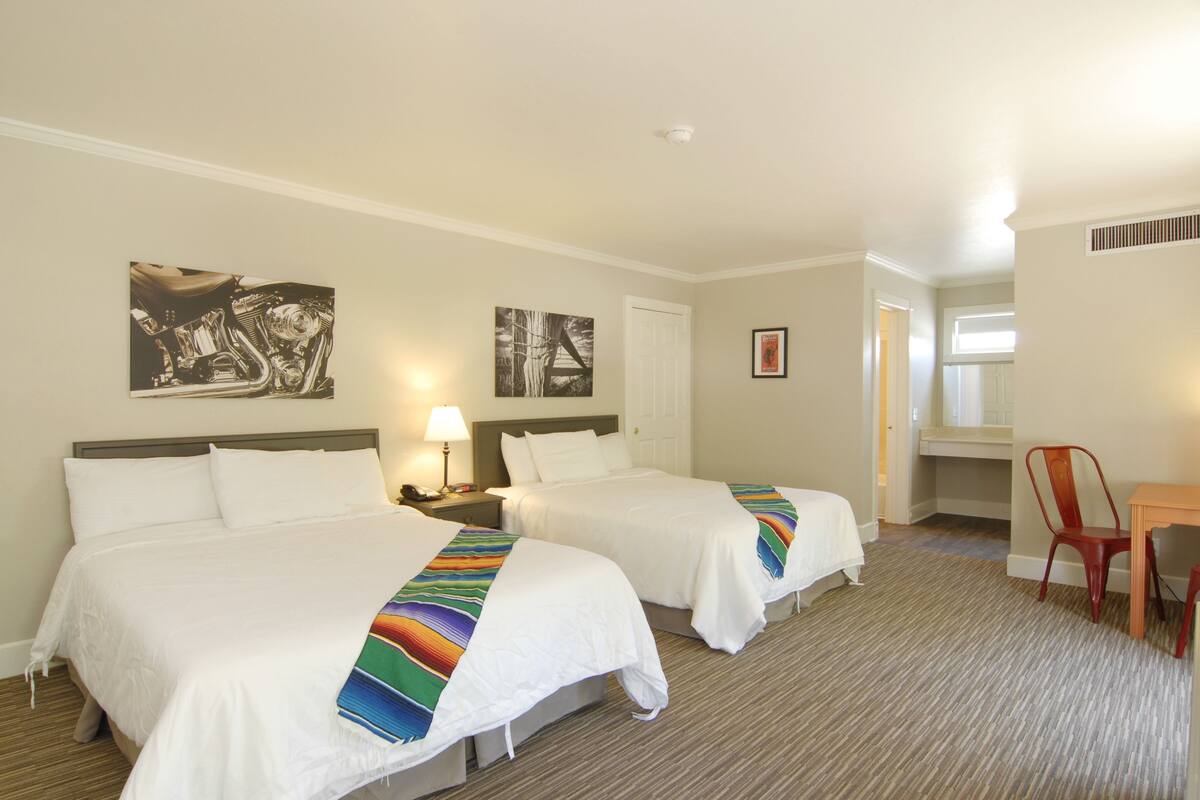 A hotel room with two beds, a desk, a chair, and artwork on the walls.