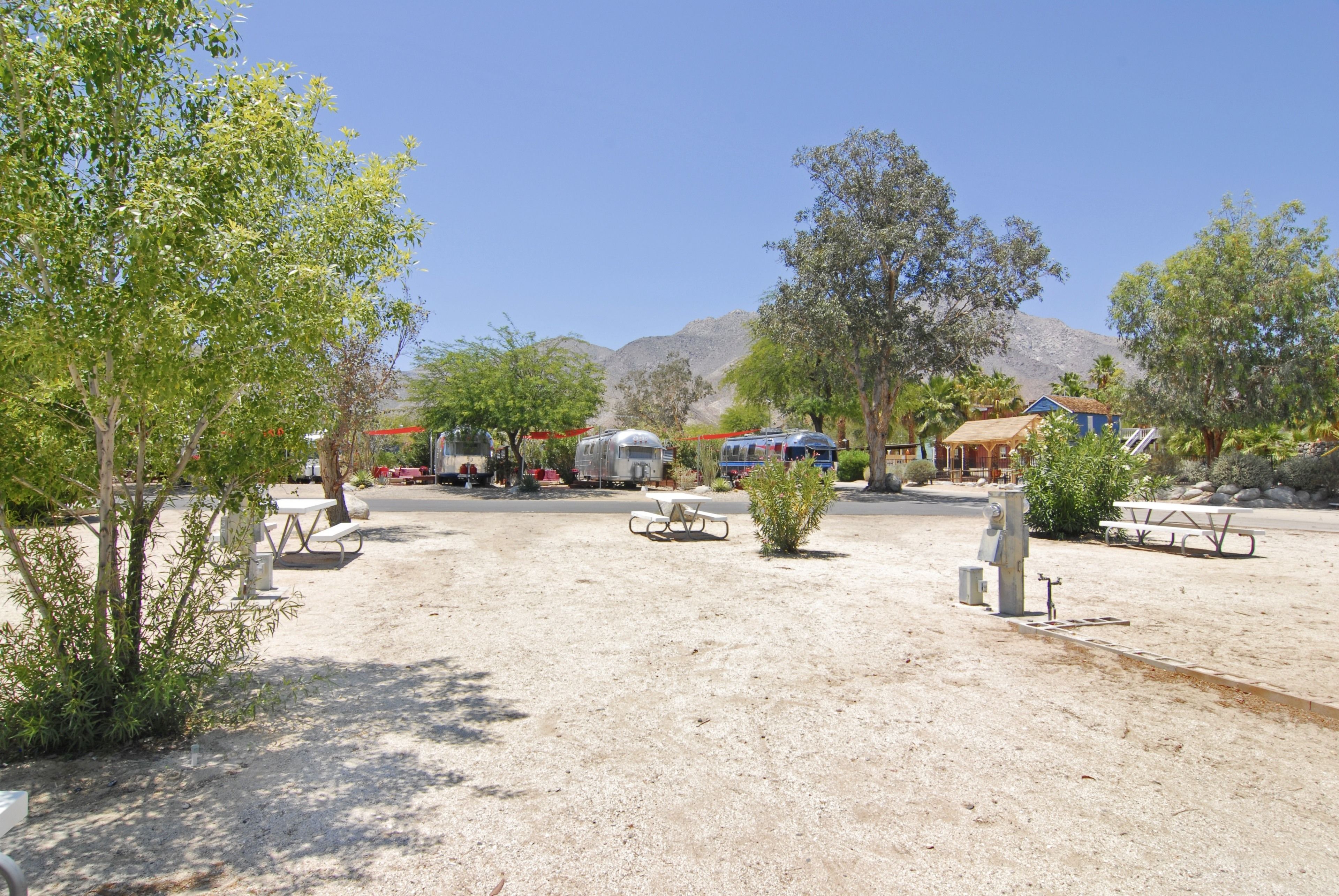 A campground with picnic tables, a water fountain, and RVs parked in the background.