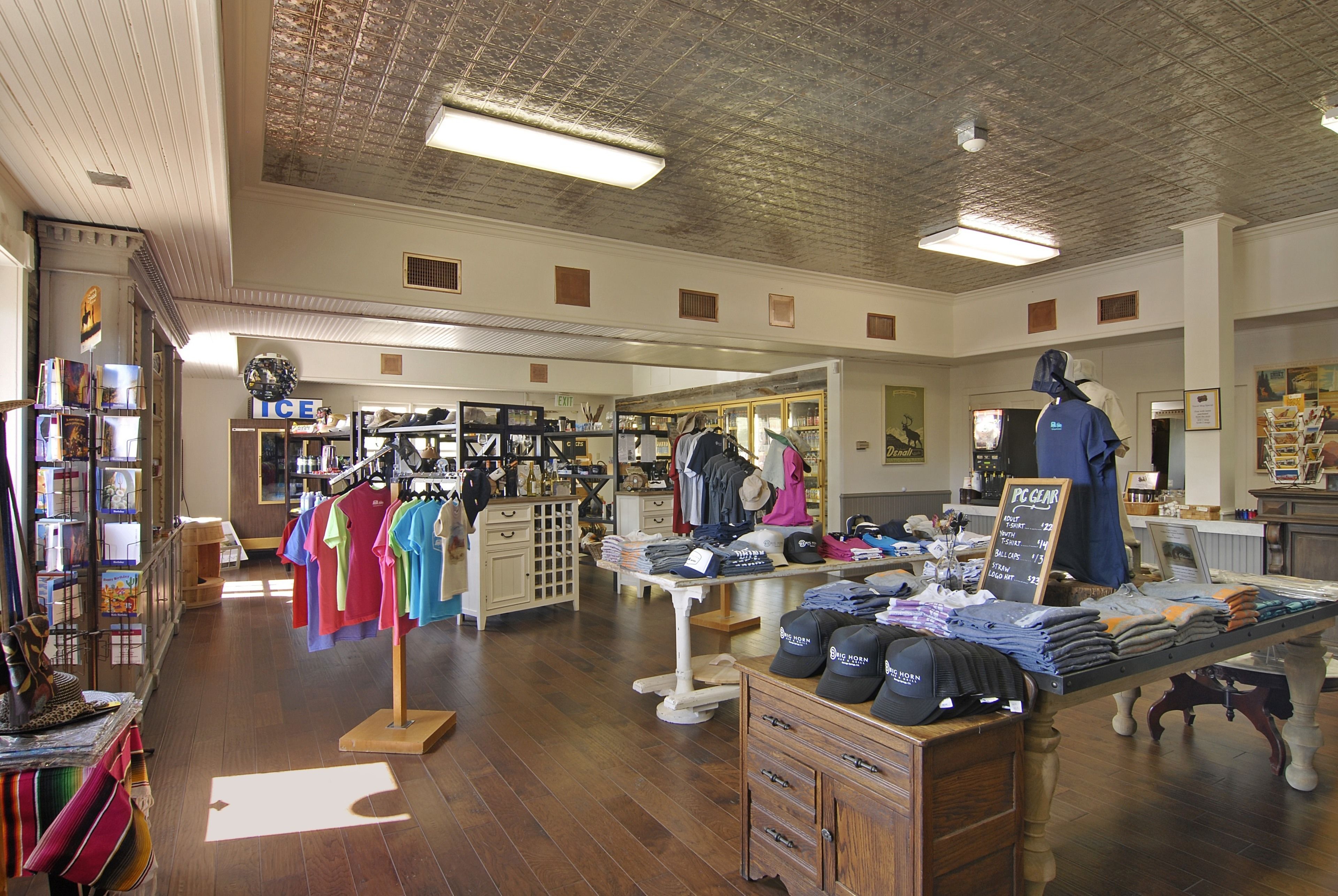 A clothing store with racks of colorful shirts, a display table with folded clothes and hats, and a mannequin in the background.