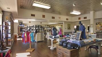 A clothing store with racks of colorful shirts, a display table with folded clothes and hats, and a mannequin in the background.