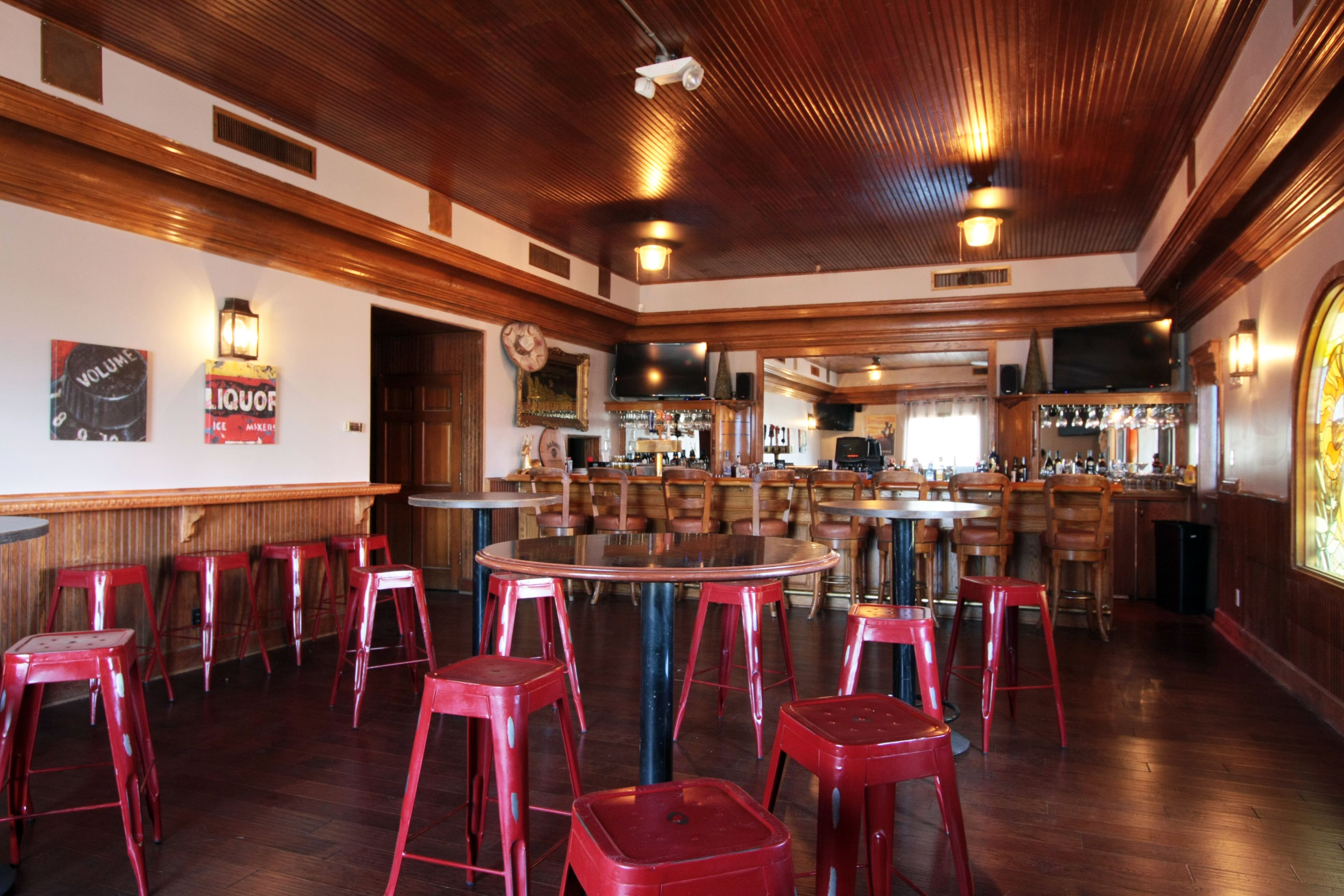 Eine Bar mit Holzbalkendecke, roten Barhocker und einer Bar mit Fernseher.