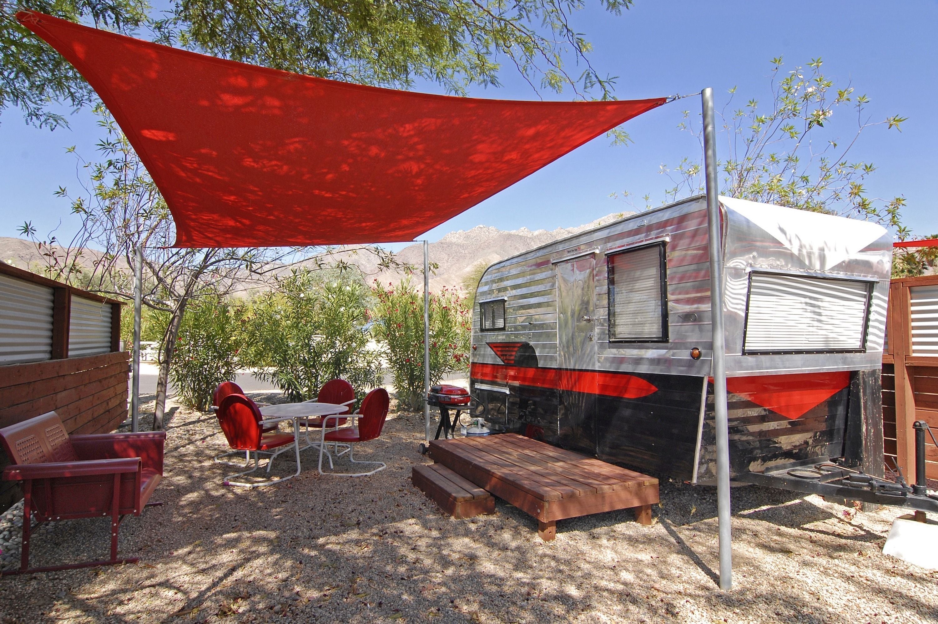 A caravan with a covered patio area, red chairs, and a table.