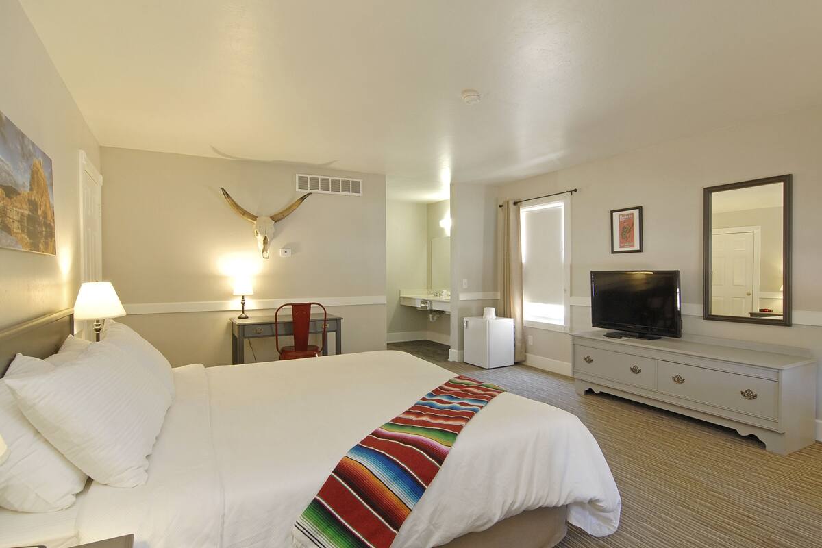 A hotel room with a large bed, a television, a dresser, a desk, and a mirror.