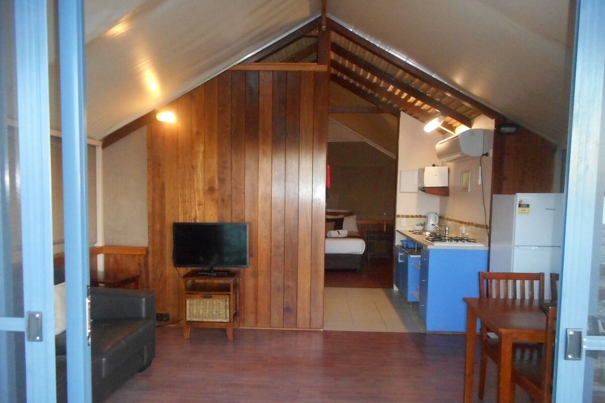 A compact, wood-paneled room with a television, kitchenette, and a small dining area.