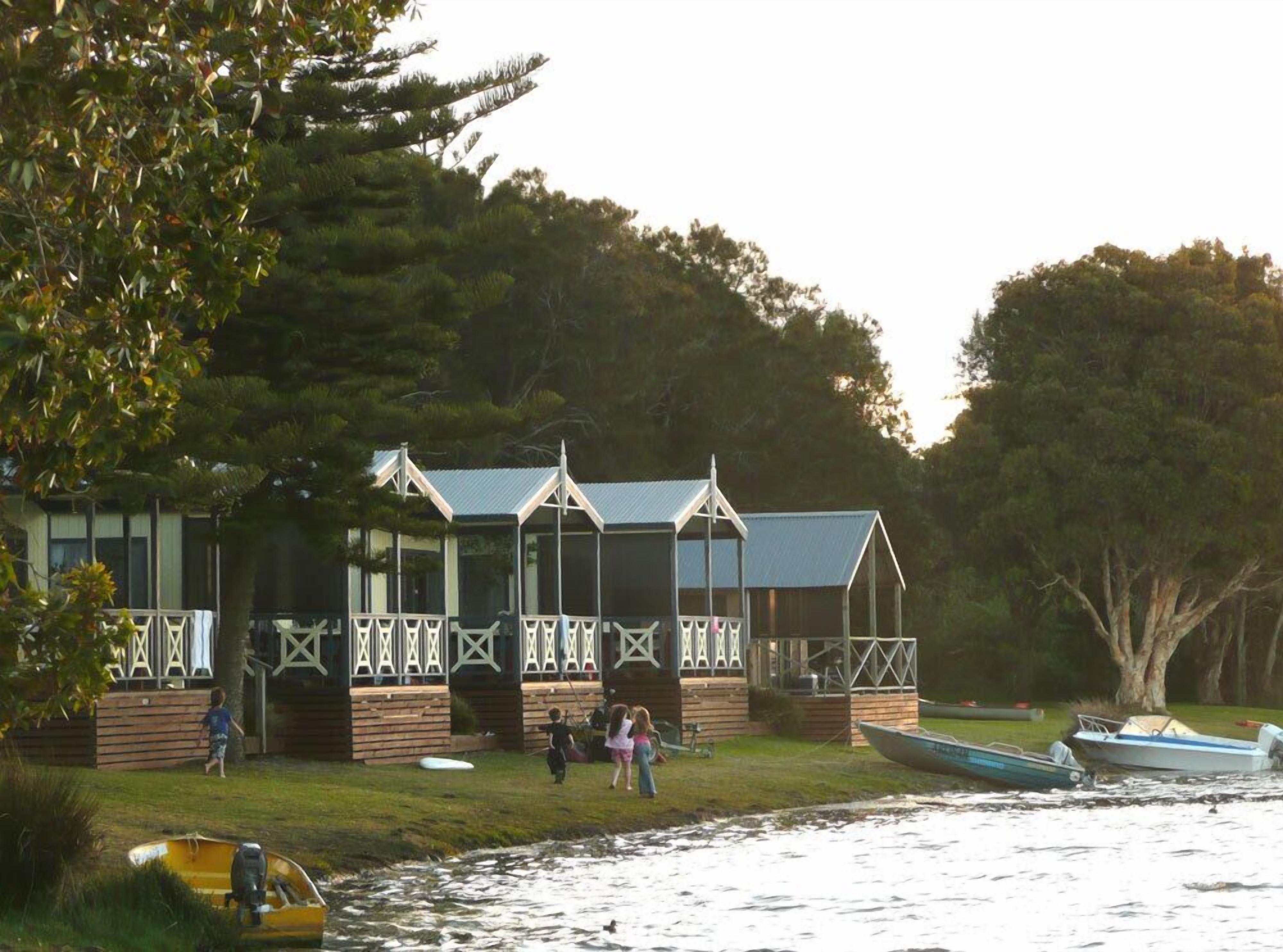 A wooden building with a covered porch, located near a body of water with boats.