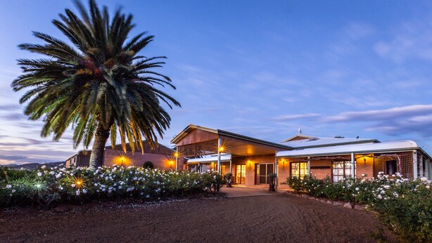 A large house with a covered porch, surrounded by white flowering plants and a palm tree. - Strathearn Park Lodge (Scone)