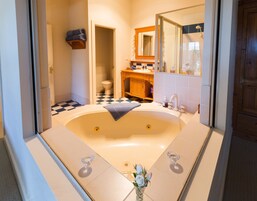 Un baño con una bañera grande, un tocador de madera, un espejo y un piso a cuadros.
