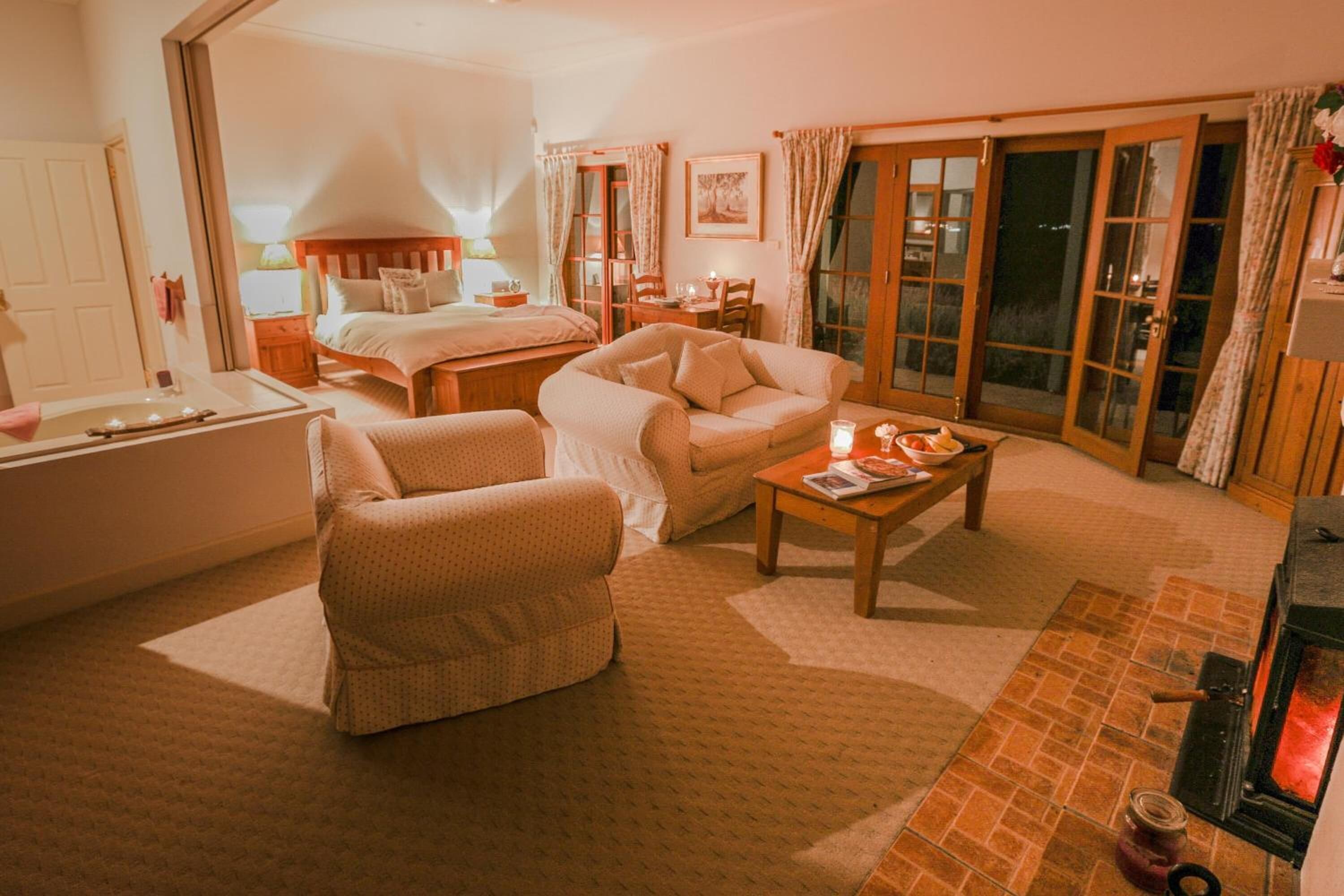 A cozy room with a bed, a sofa, a small table, a fireplace, and a sliding glass door leading to an outdoor area.