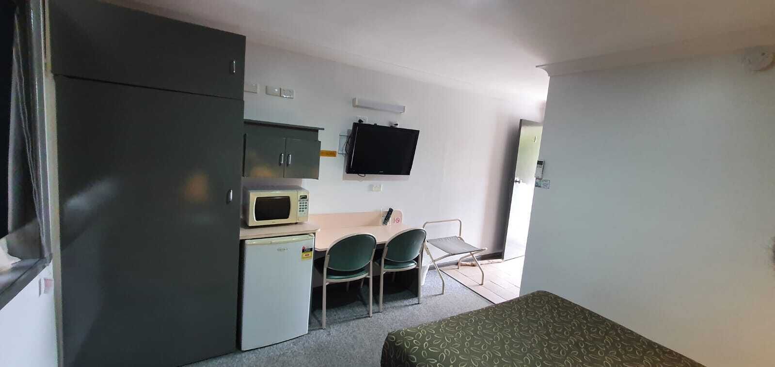 A compact room with a bed, kitchenette, two chairs, a TV, and a door.
