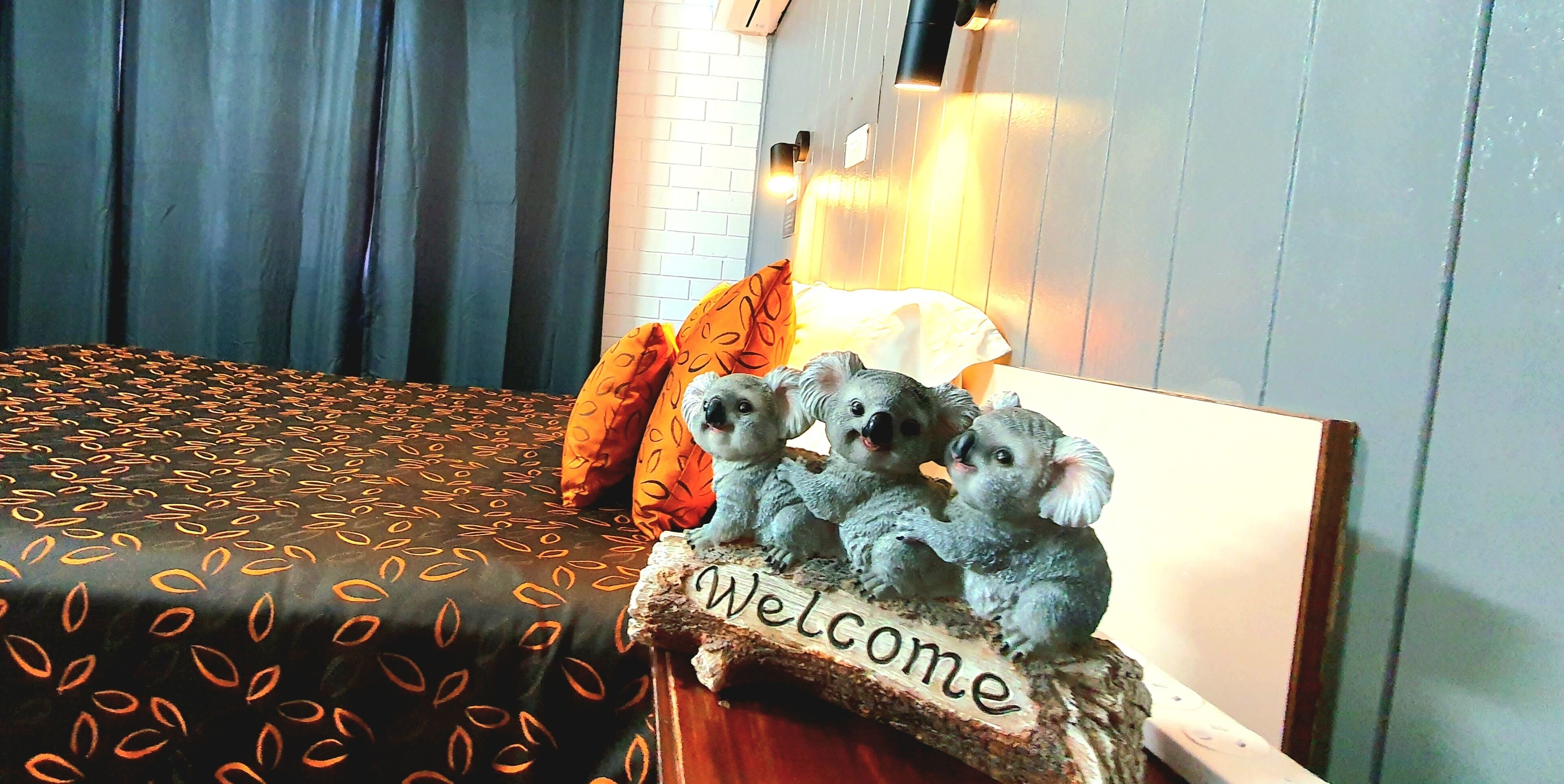 A bed with a patterned bedspread, a 'Welcome' sign, and a lamp.
