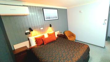 A hotel room with a bed, a chair, a nightstand, and a wall-mounted air conditioner.