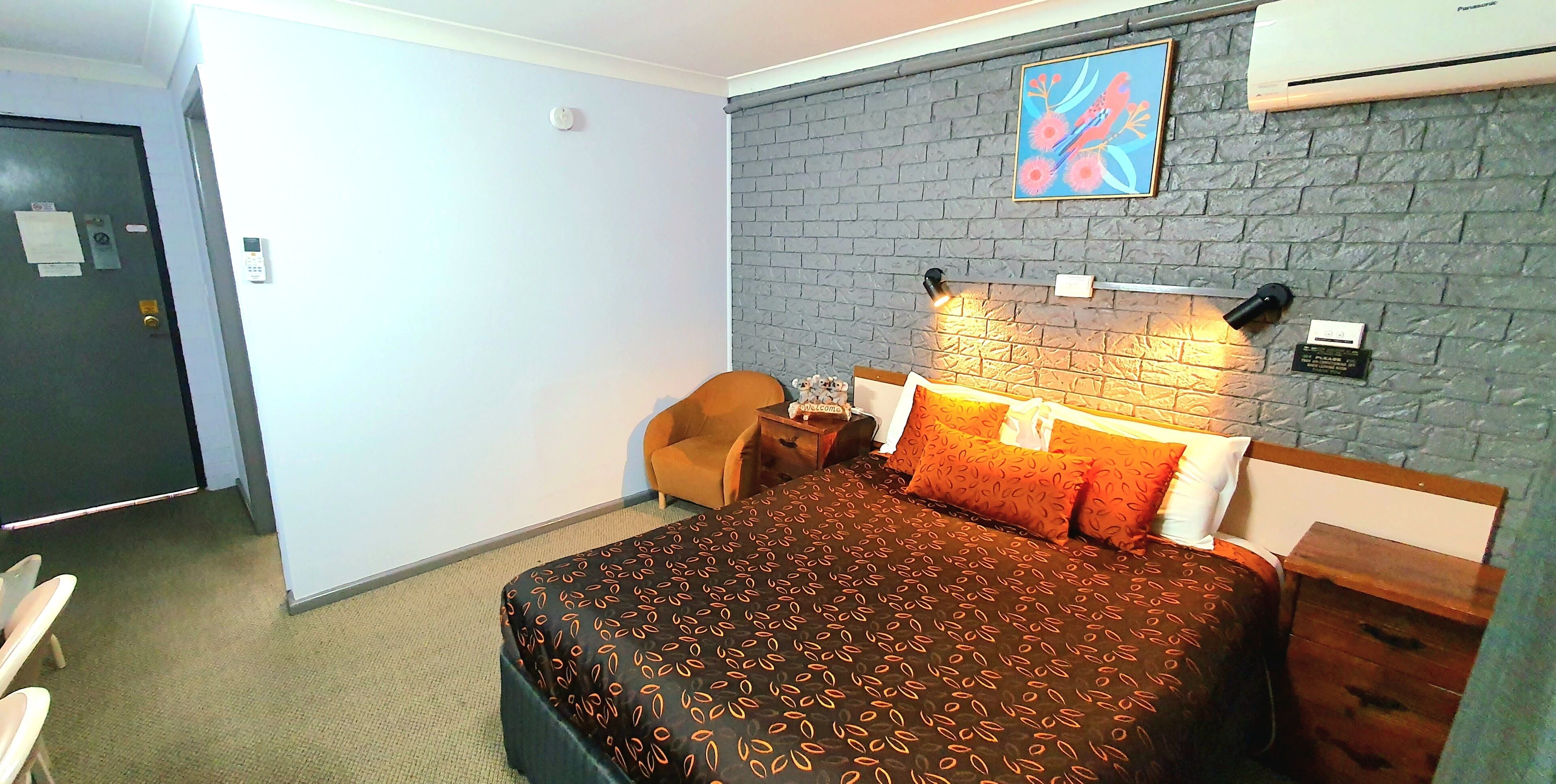 Habitación de hotel con una cama, una silla, un escritorio y un aire acondicionado instalado en la pared.